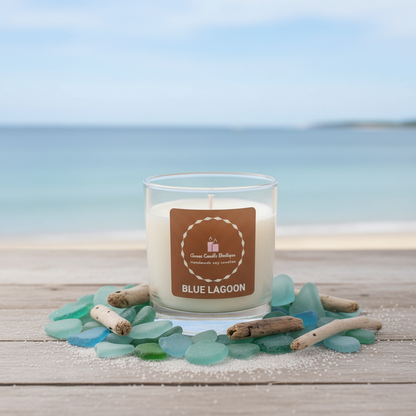 Candle labeled 'Blue Lagoon' with sea glass and driftwood on a beach setting