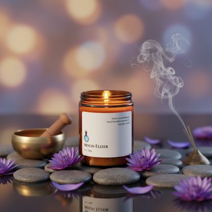 Candle labeled 'Moon Elixir' with purple flowers and stones on a blurred background