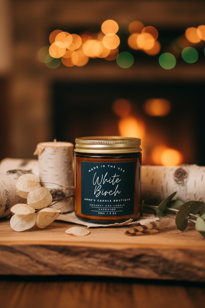 Candle labeled 'White Birch' on a wooden surface with a fireplace in the background